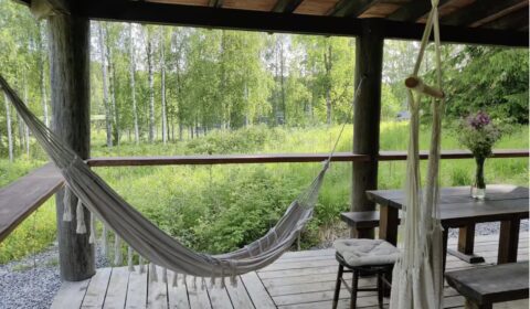 Vuokrattavan hirsimökin terassilla oleva riippukeinu luonnon ympäröimänä